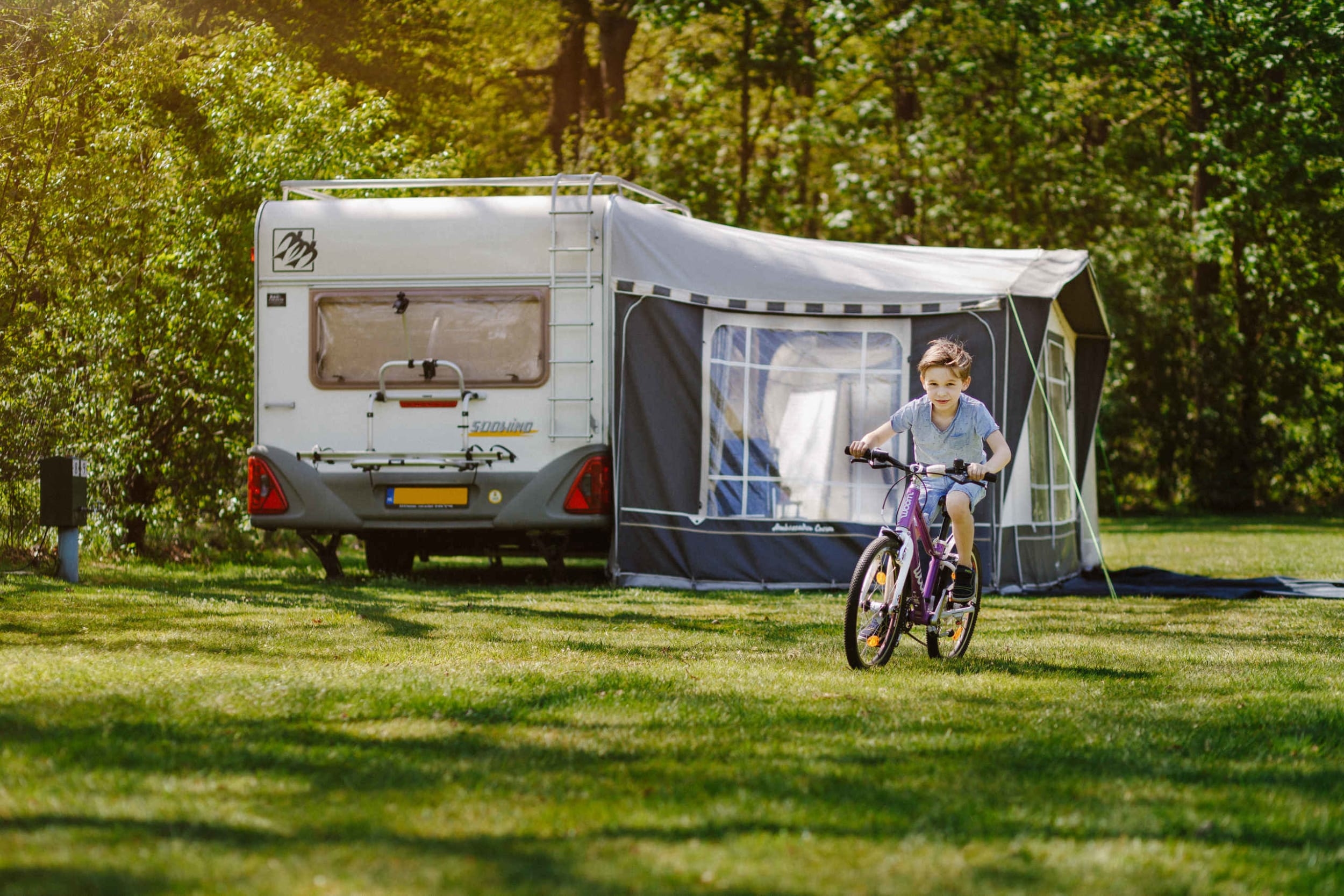 kampeerplaats-jongen-fietsen-caravan-tent-kamp